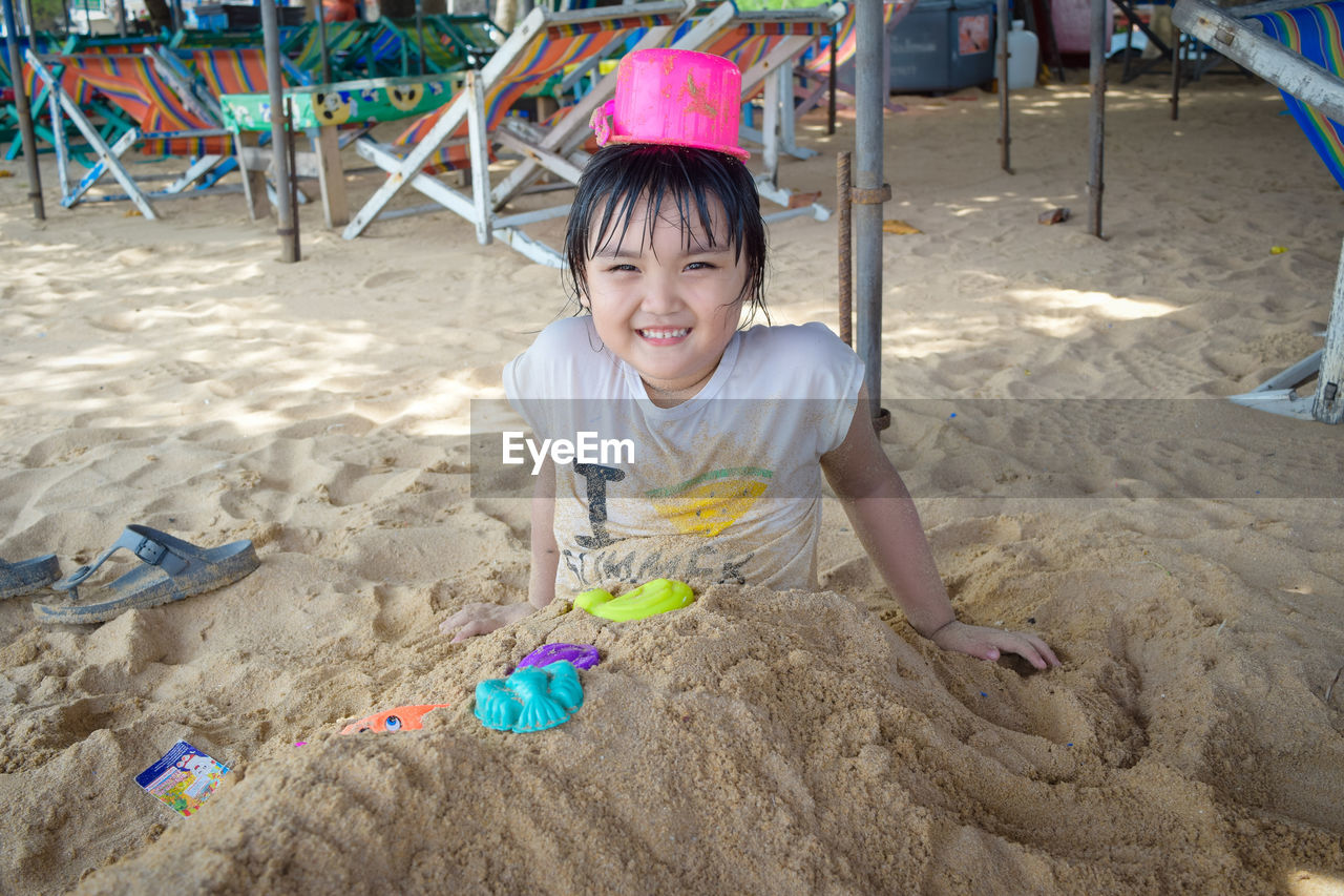 Portrait of smiling girl buried in sand at beach