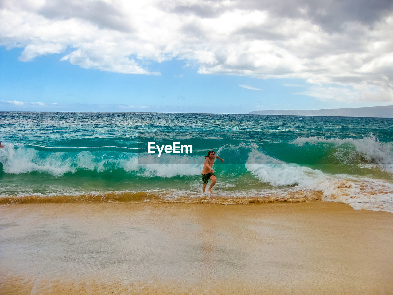 Shirtless man running at beach against cloudy sky