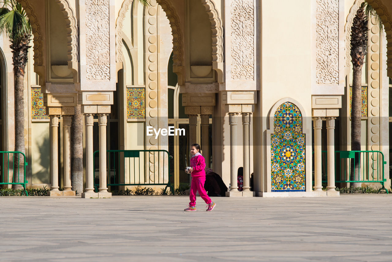 FULL LENGTH REAR VIEW OF WOMAN STANDING AGAINST BUILDING