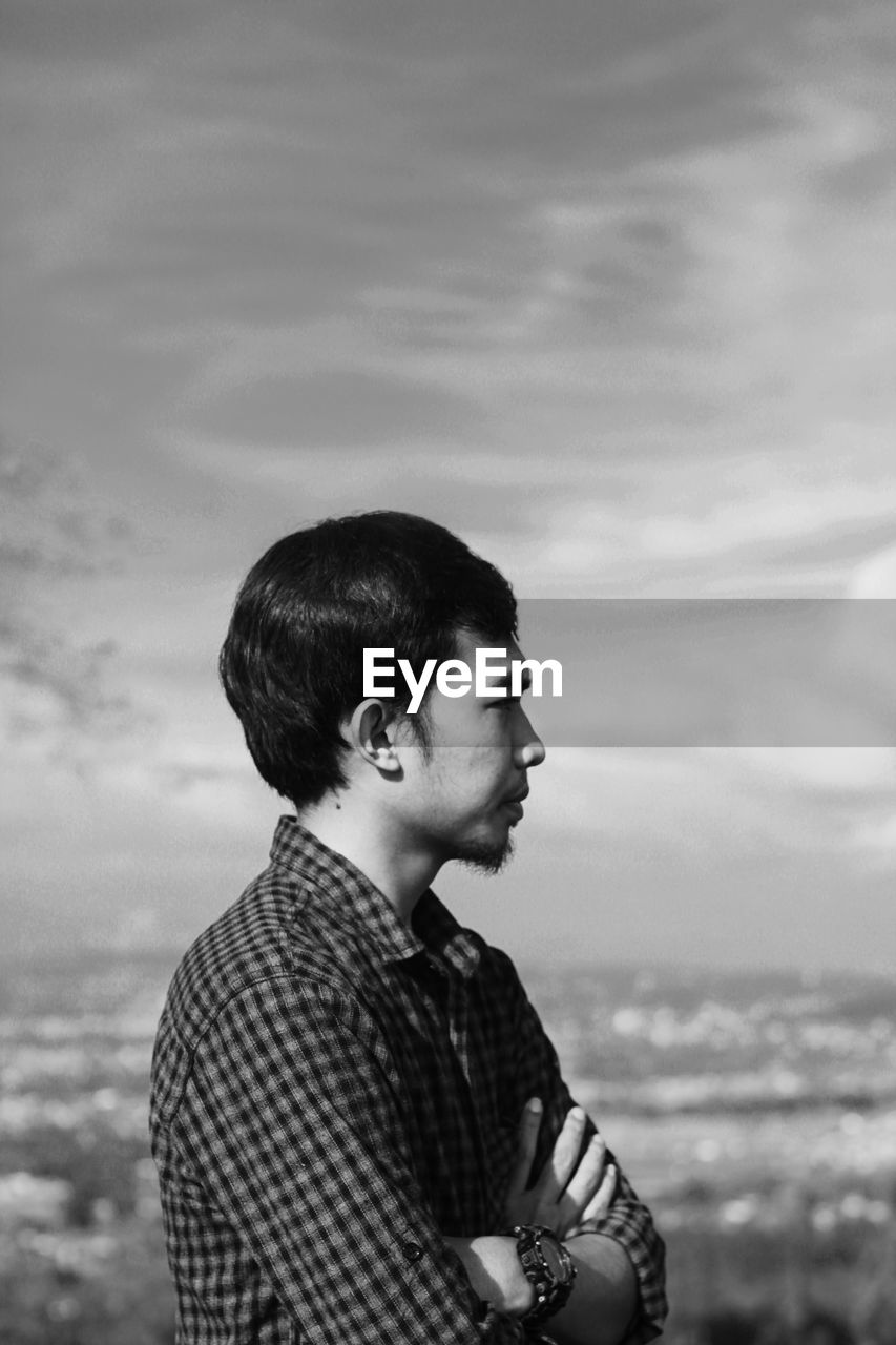 Side view of young man looking at sea against sky