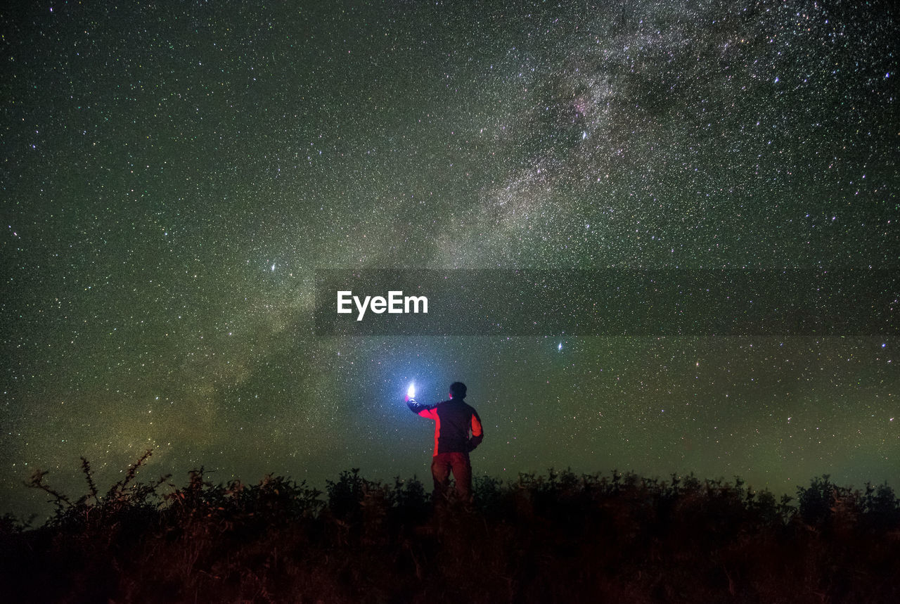 Rear view of man with illuminated flashlight standing against star field