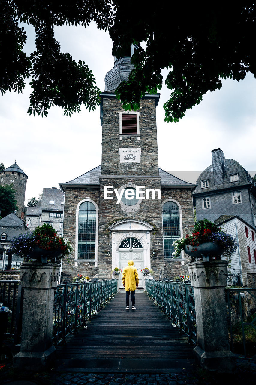 REAR VIEW OF WOMAN WALKING AMIDST BUILDINGS AND TREES AGAINST SKY