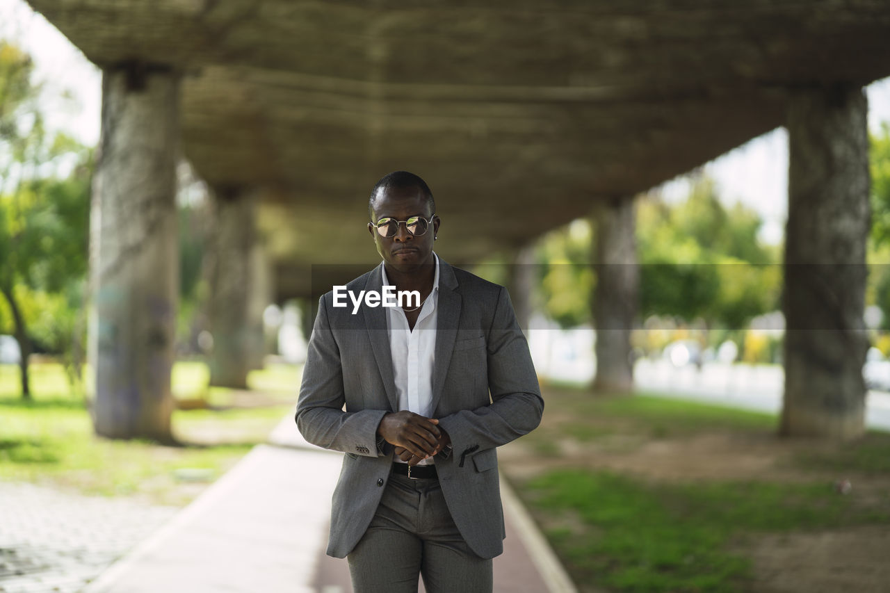 Masculine african american male executive in formal suit and sunglasses revising time on street