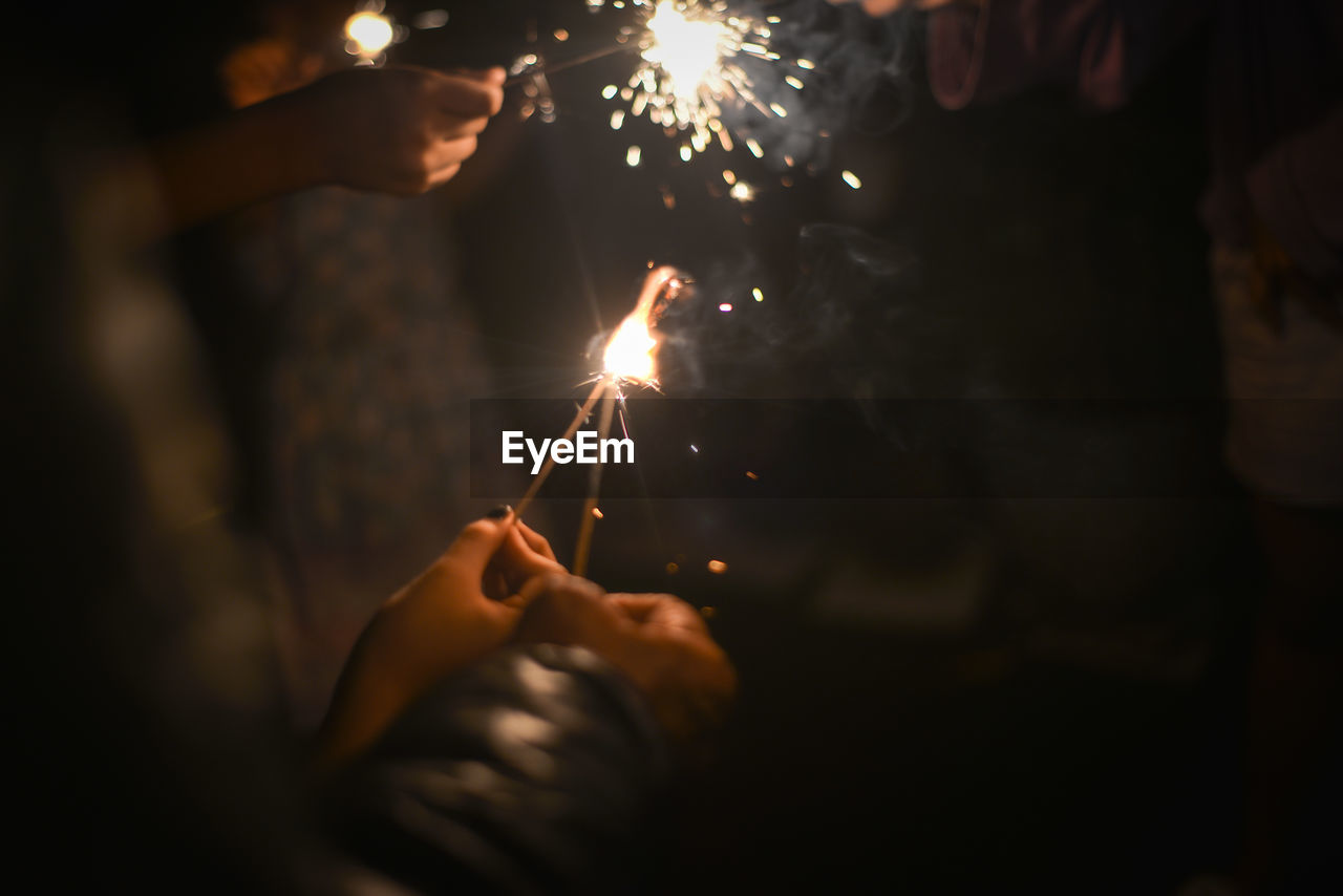 Cropped hand holding sparkler at night