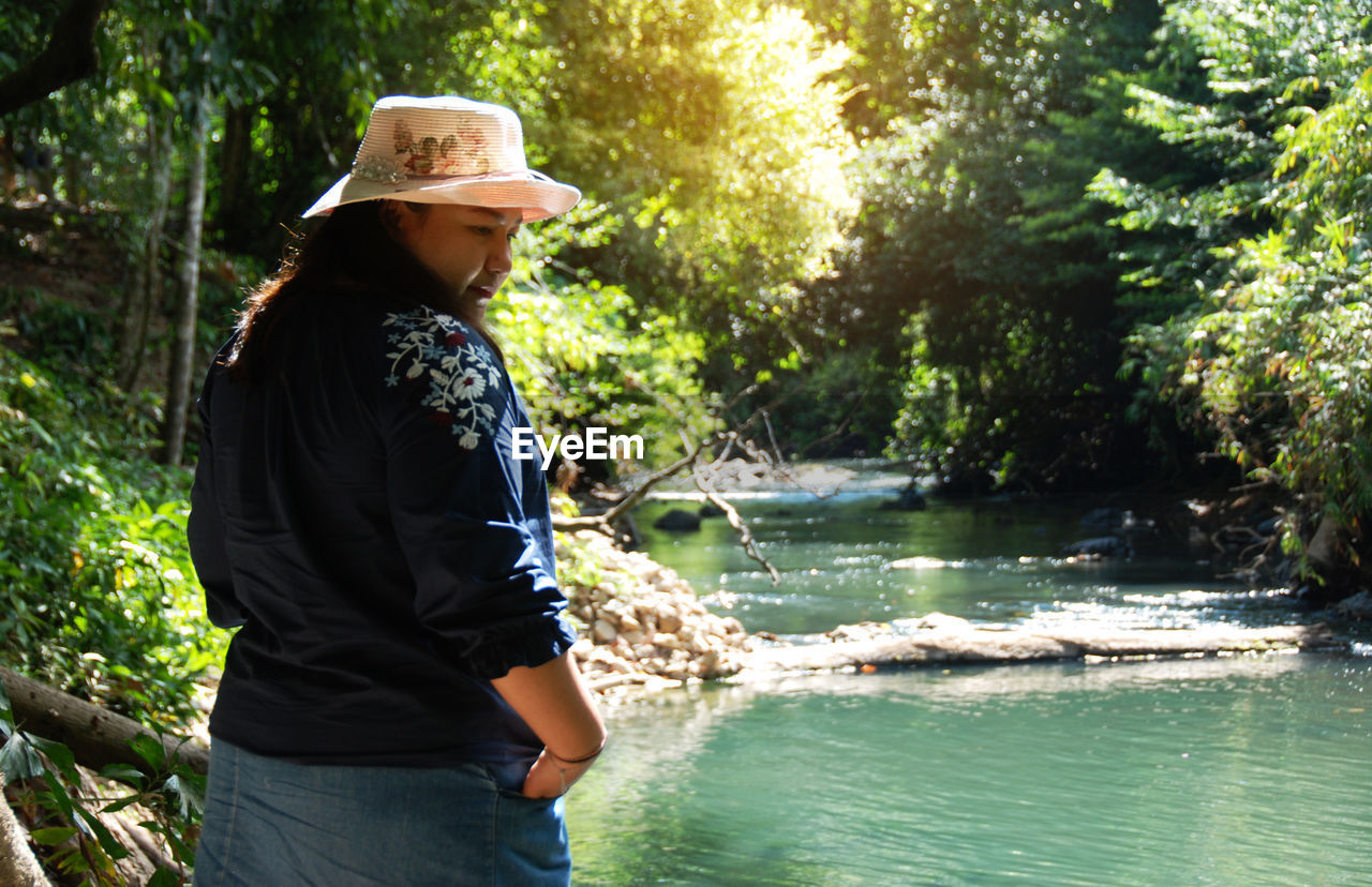 Woman wearing hat and looking away while standing by river
