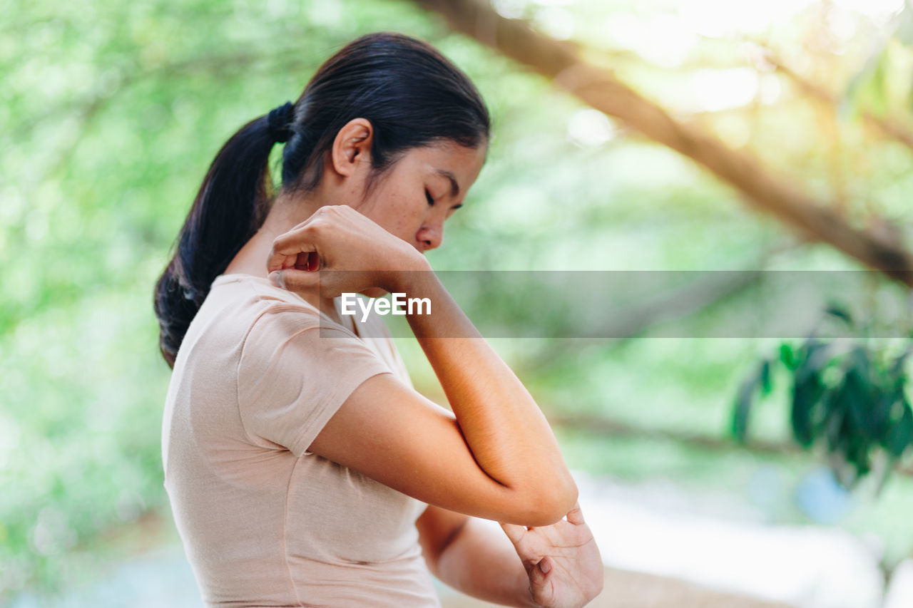 Side view of woman touching elbow against tree