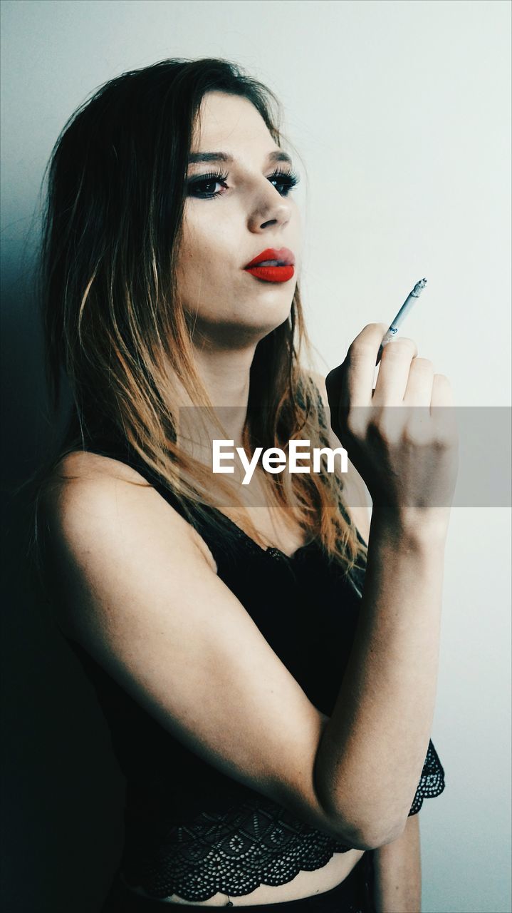 Young woman smoking cigarette while standing by wall