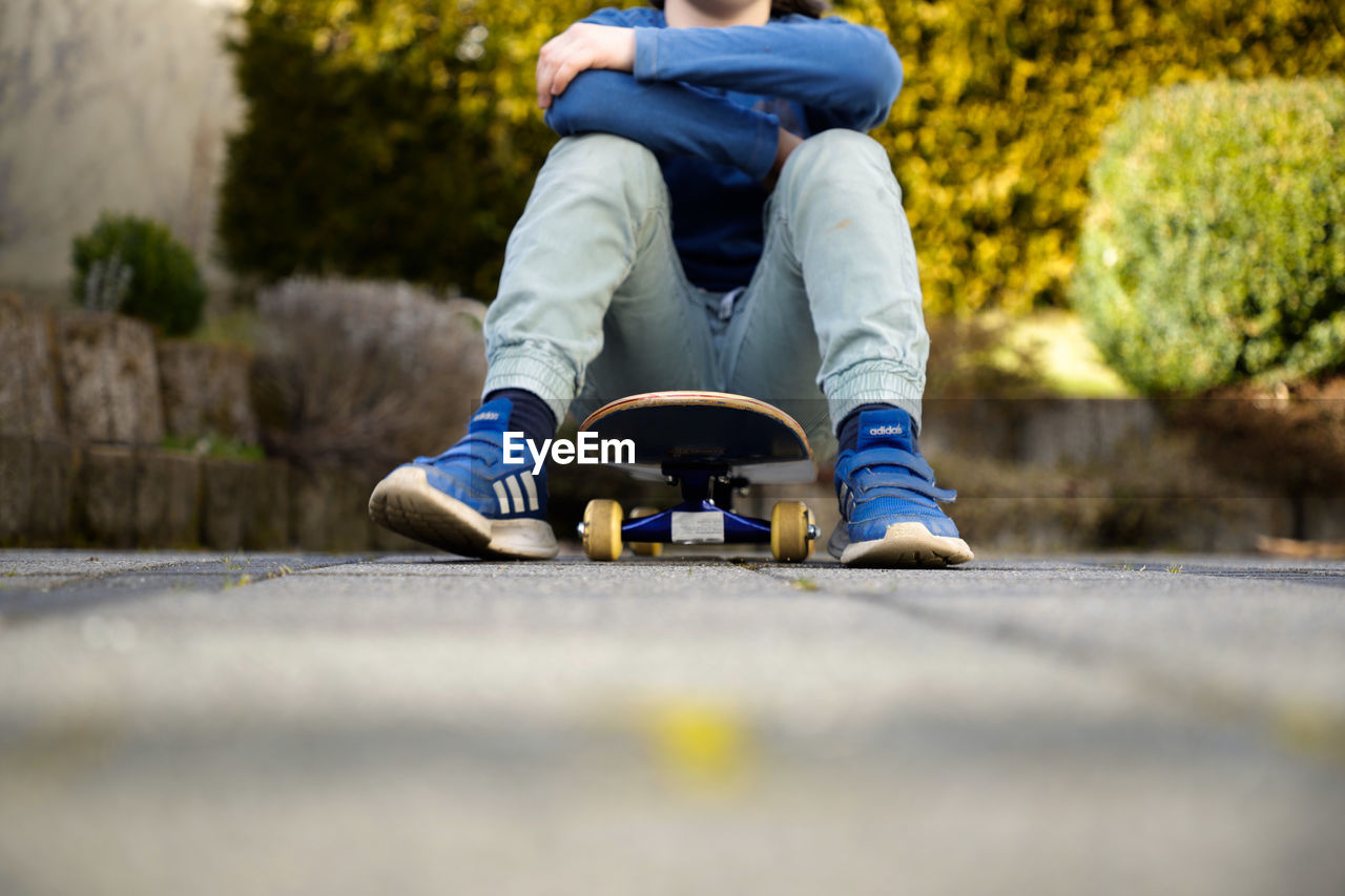 LOW SECTION OF BOY SITTING ON SKATEBOARD OUTDOORS