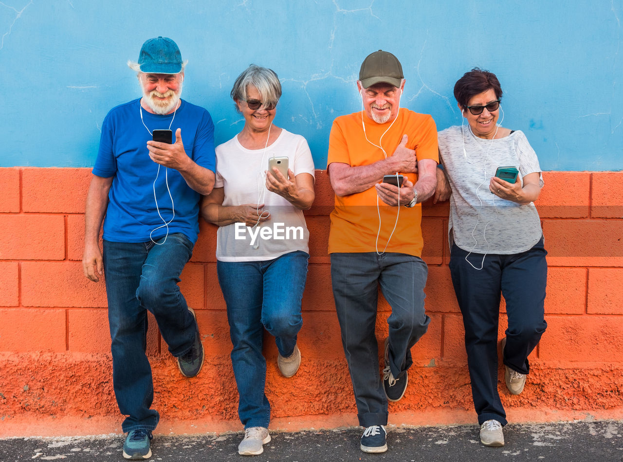 Senior people listening to music while standing against wall 