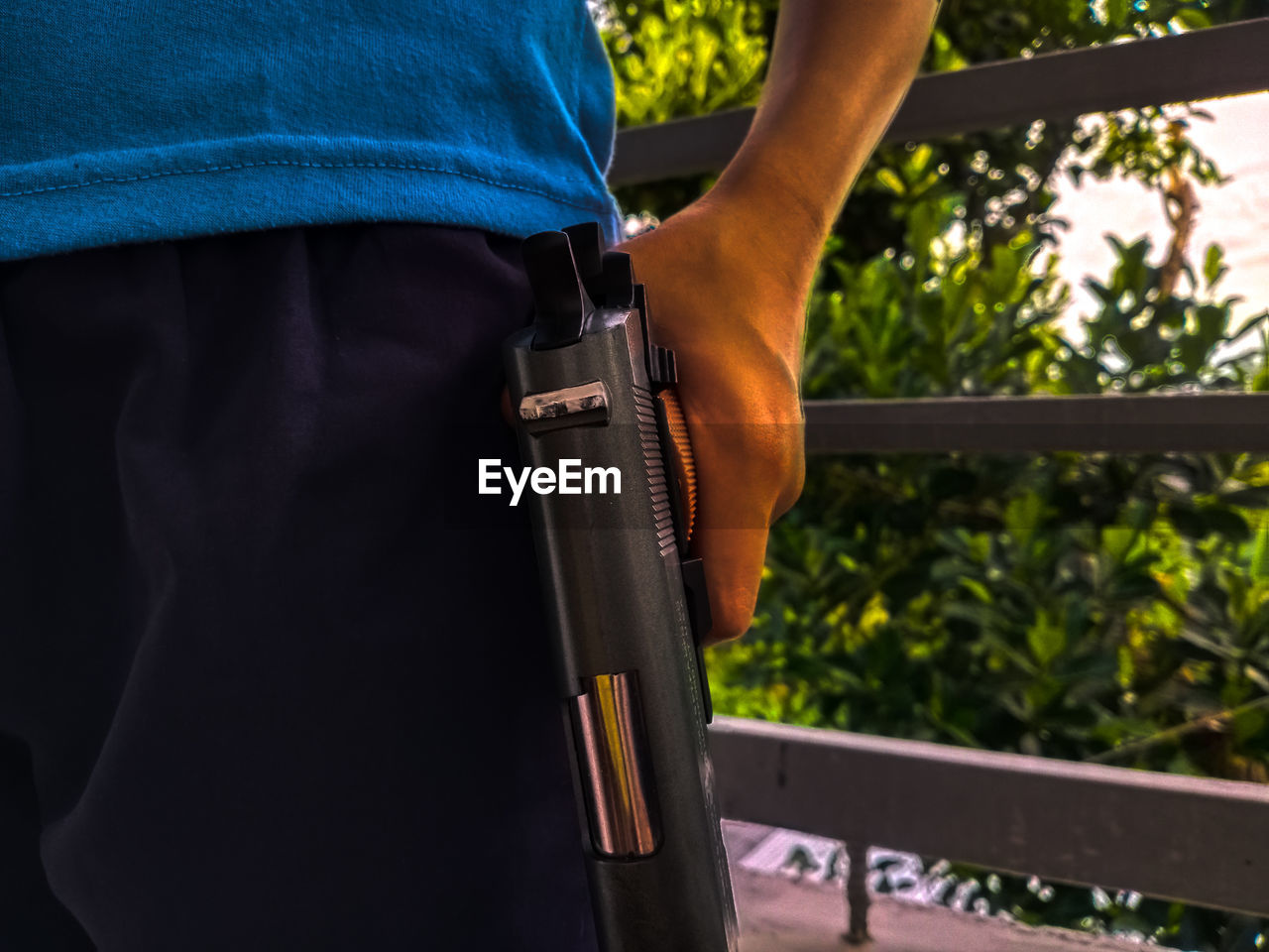 MIDSECTION OF MAN HOLDING CAMERA WHILE STANDING ON OUTDOORS