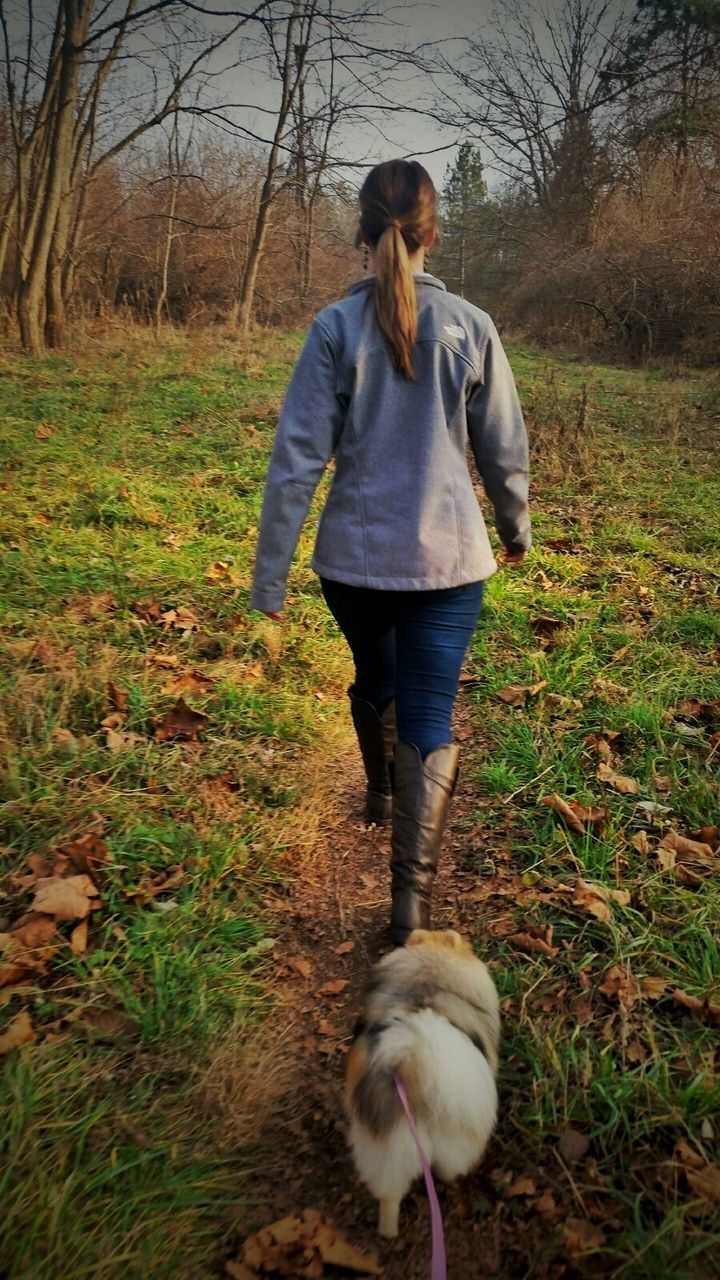 Rear view of woman walking with dog on grassy field