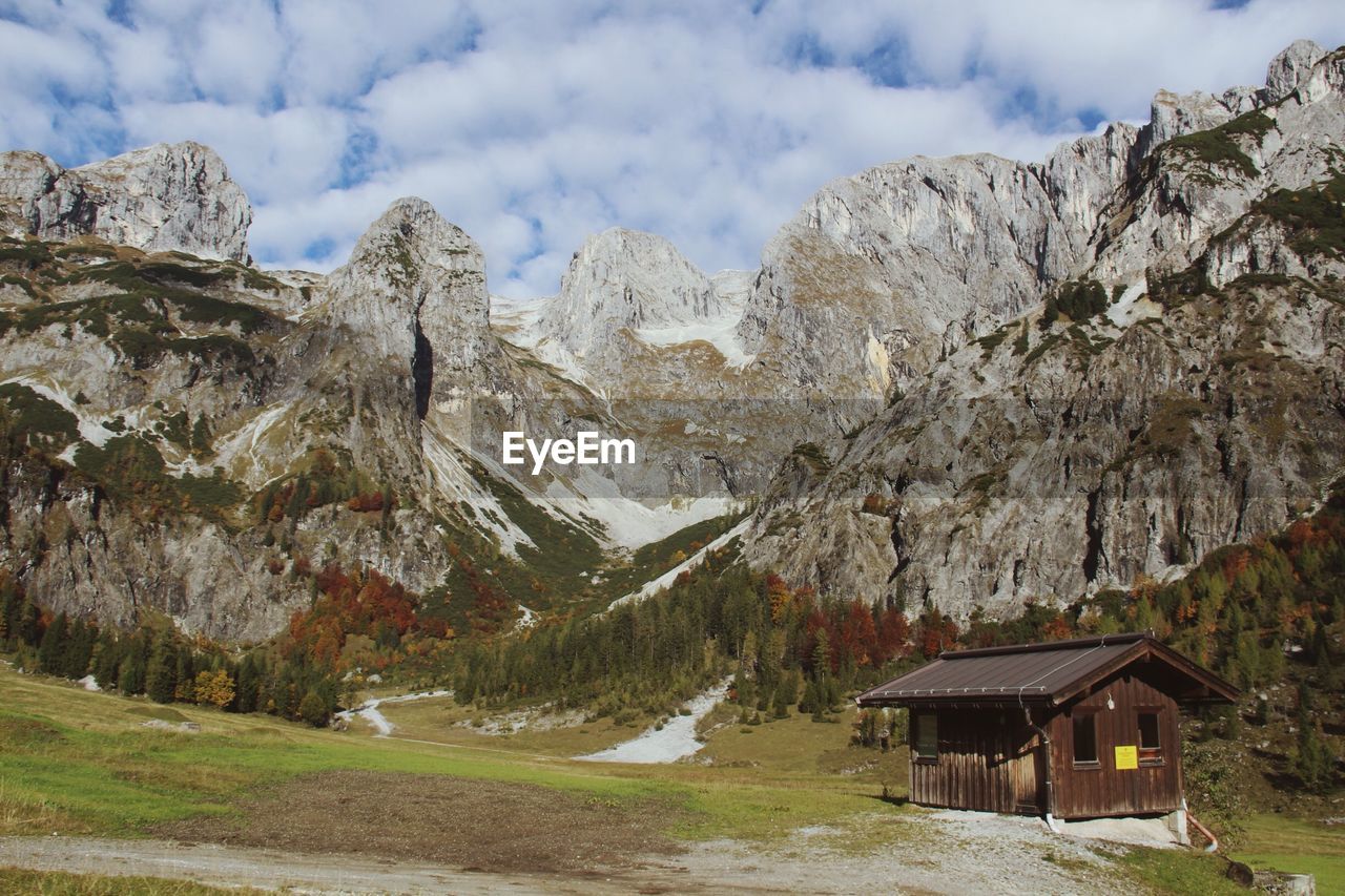 Hut on field against rocky mountains