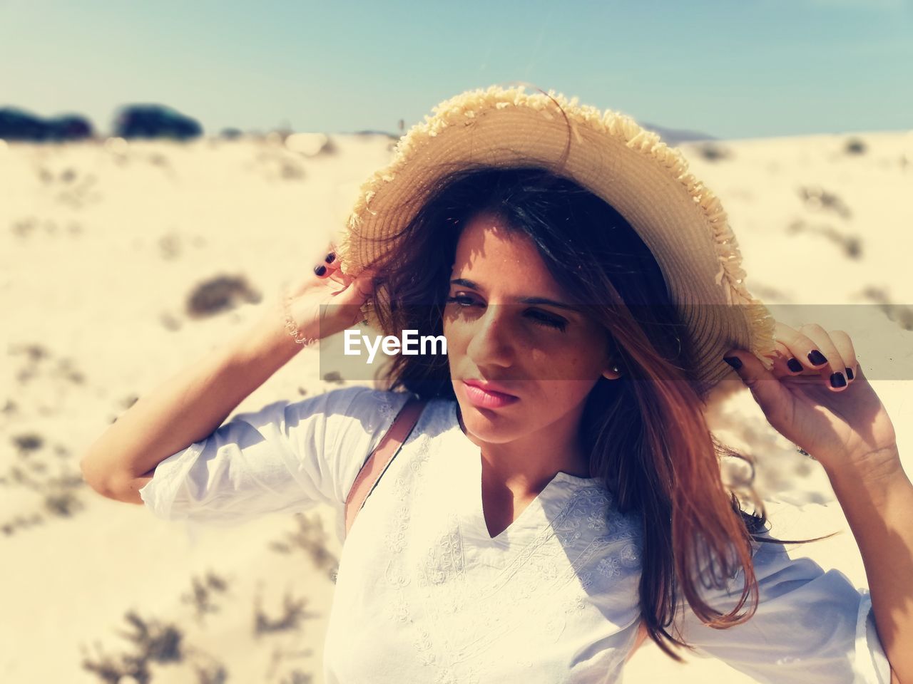 Beautiful young woman holding hat at beach on sunny day