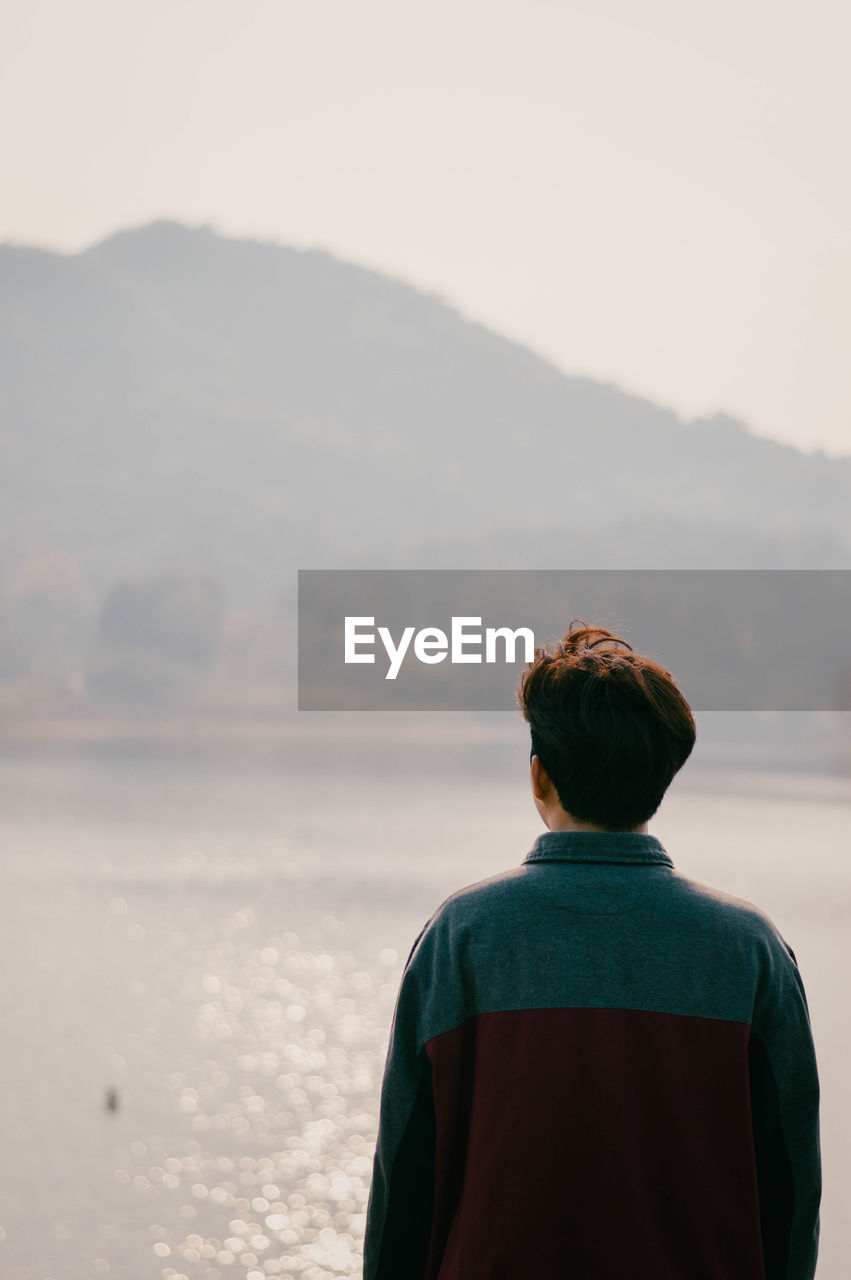 REAR VIEW OF MAN LOOKING AT SEA