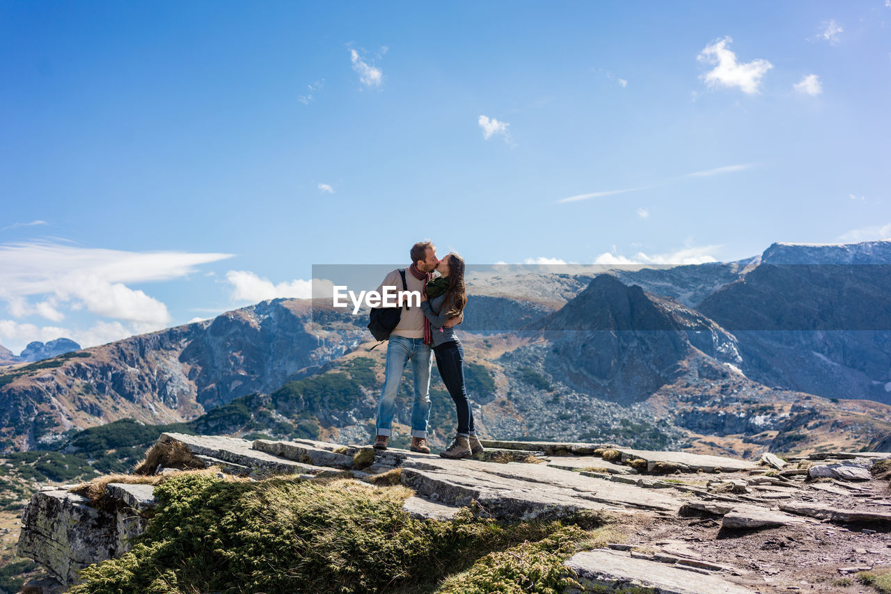Couple kissing while standing against mountain during sunny day
