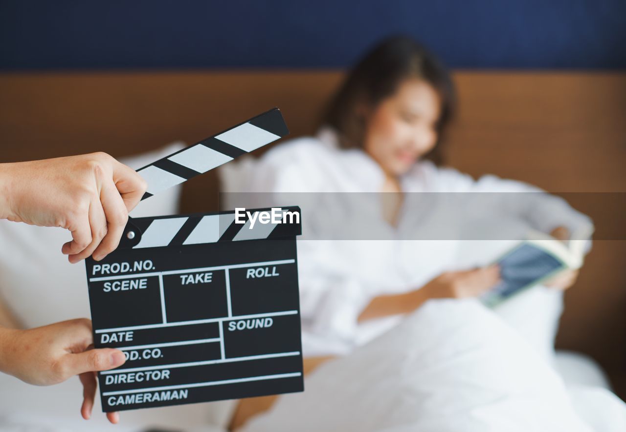 Cropped hand holding film slate against woman sitting on bed