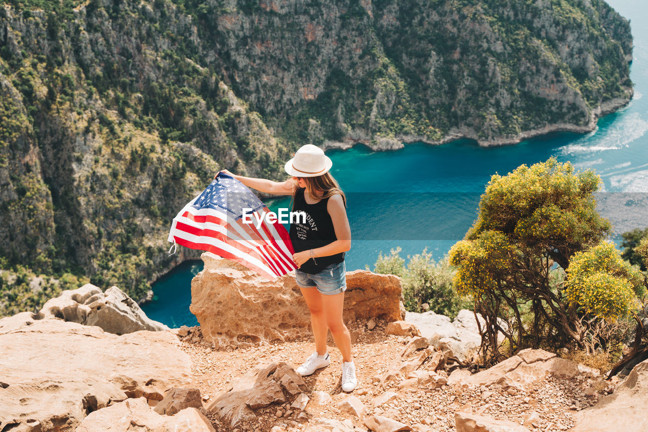 Woman standing on rock and waving  us flag. traveler standing on mountain. 4 july independence day