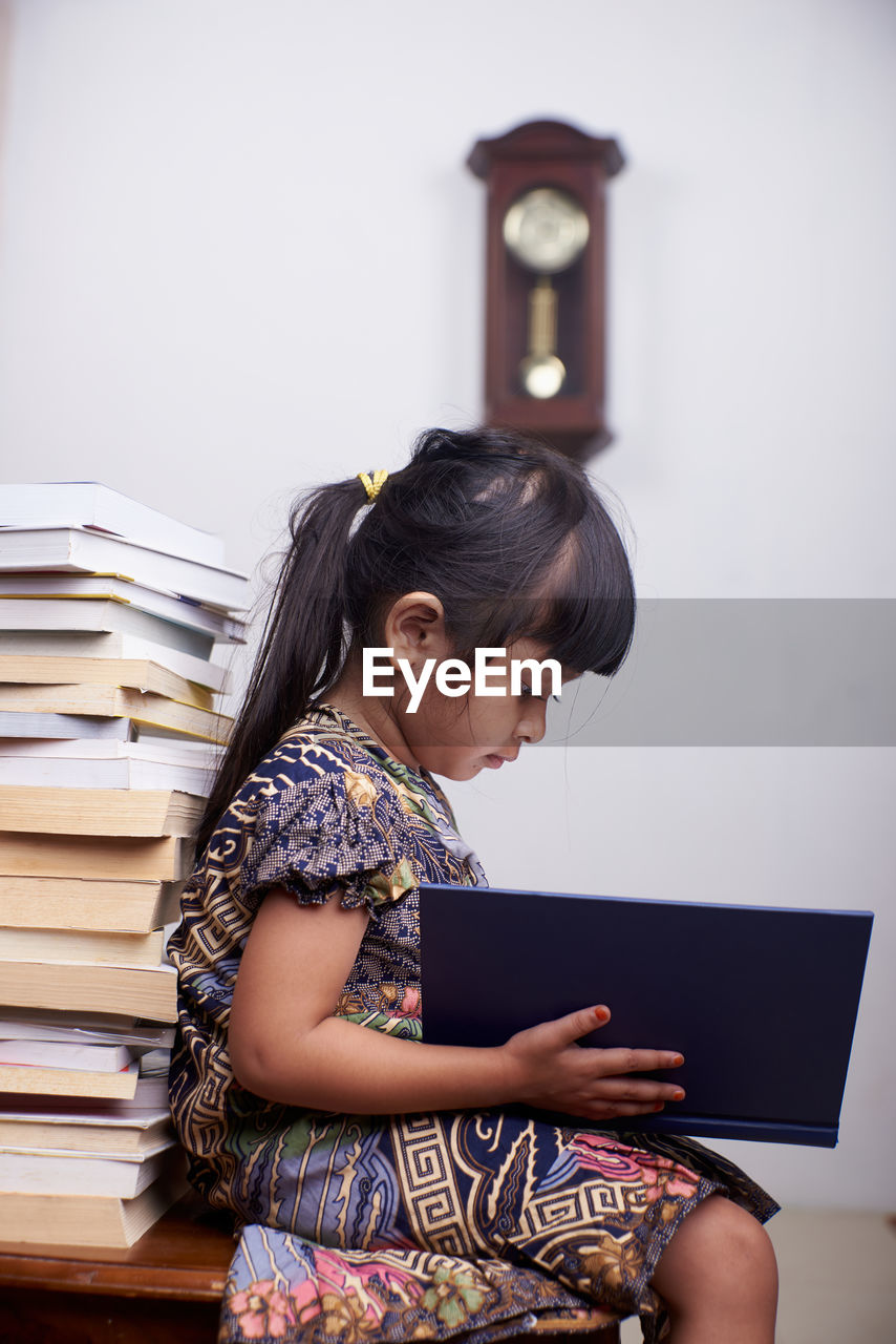 Side view of girl reading book at home