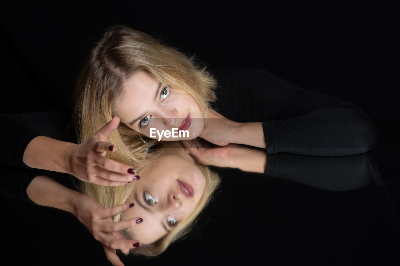 Portrait of young woman on mirror against black background