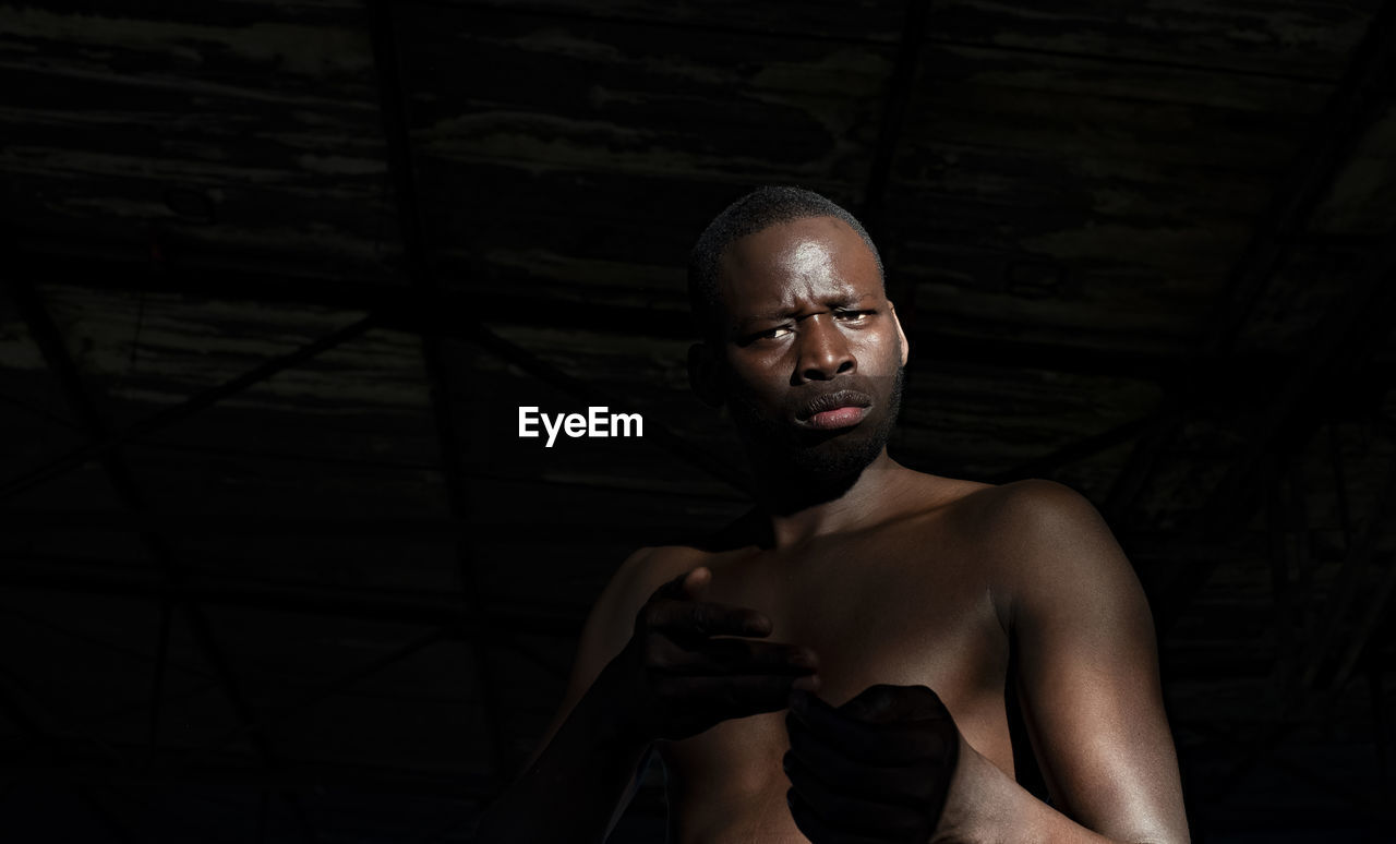 Portrait of confident shirtless man standing against black background