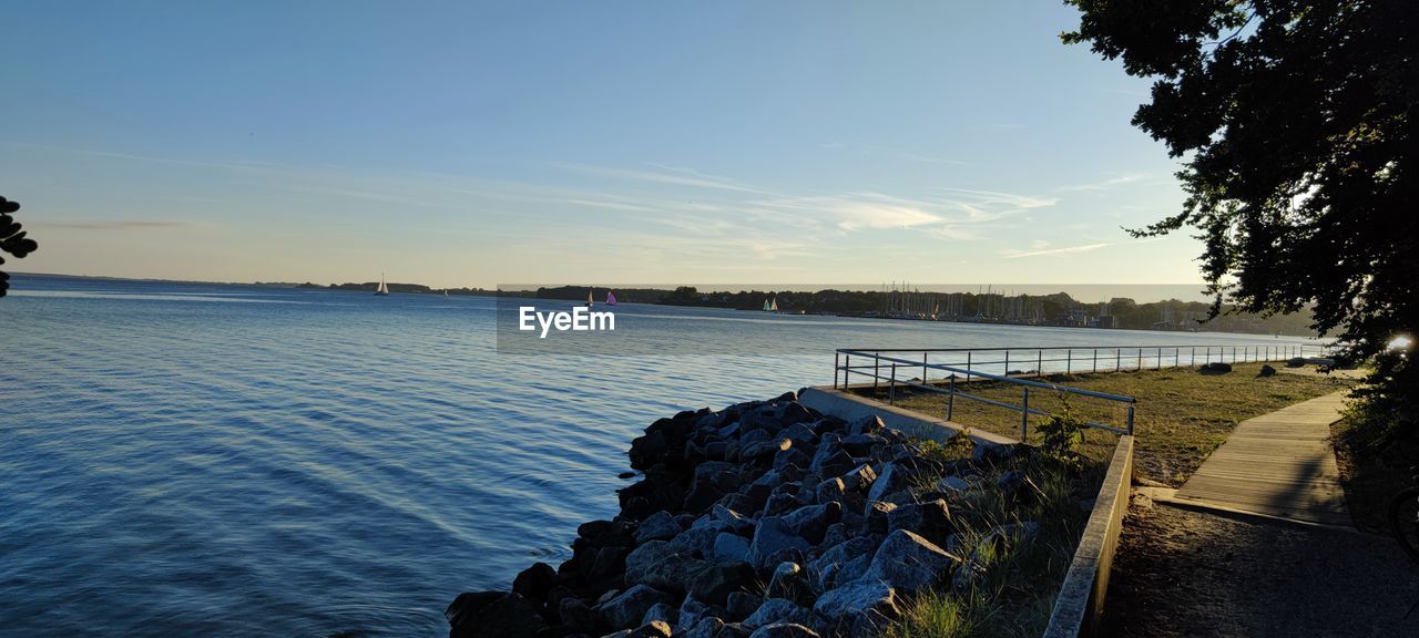 water, sky, reflection, sea, nature, shore, sunset, dusk, scenics - nature, tree, beauty in nature, evening, tranquility, body of water, coast, ocean, horizon, tranquil scene, beach, plant, land, sunlight, no people, bay, outdoors, travel destinations, blue, cloud, travel, idyllic, environment, landscape, clear sky, day, non-urban scene, architecture, transportation, coastline, vacation