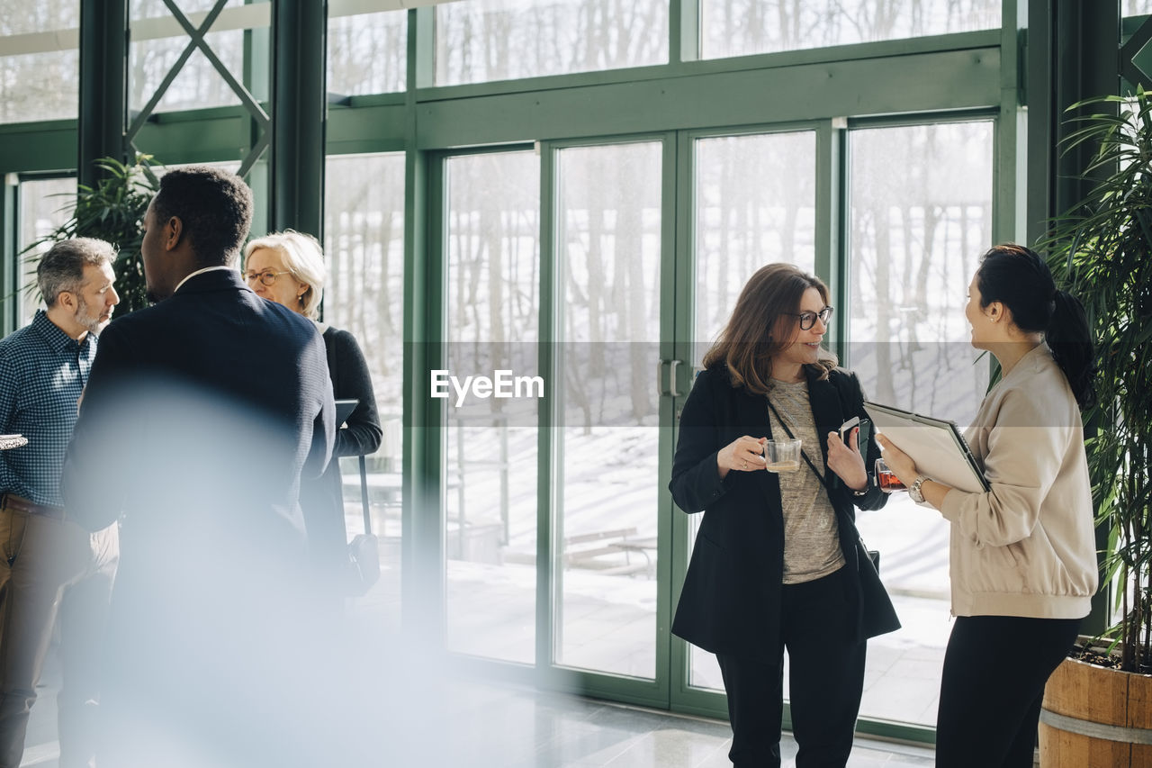 Business colleagues communicating while standing against window at office