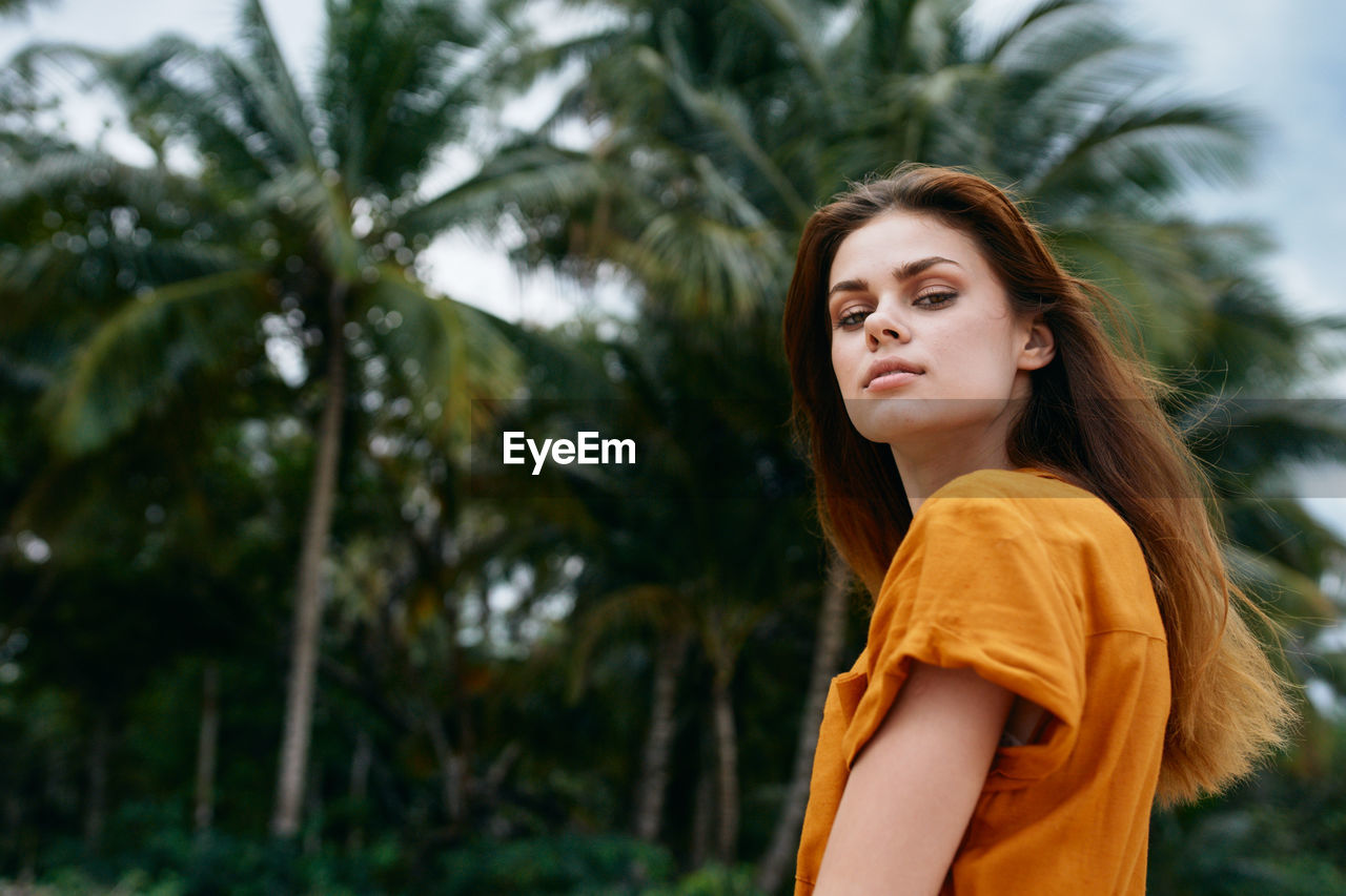 Portrait of beautiful young woman standing against trees