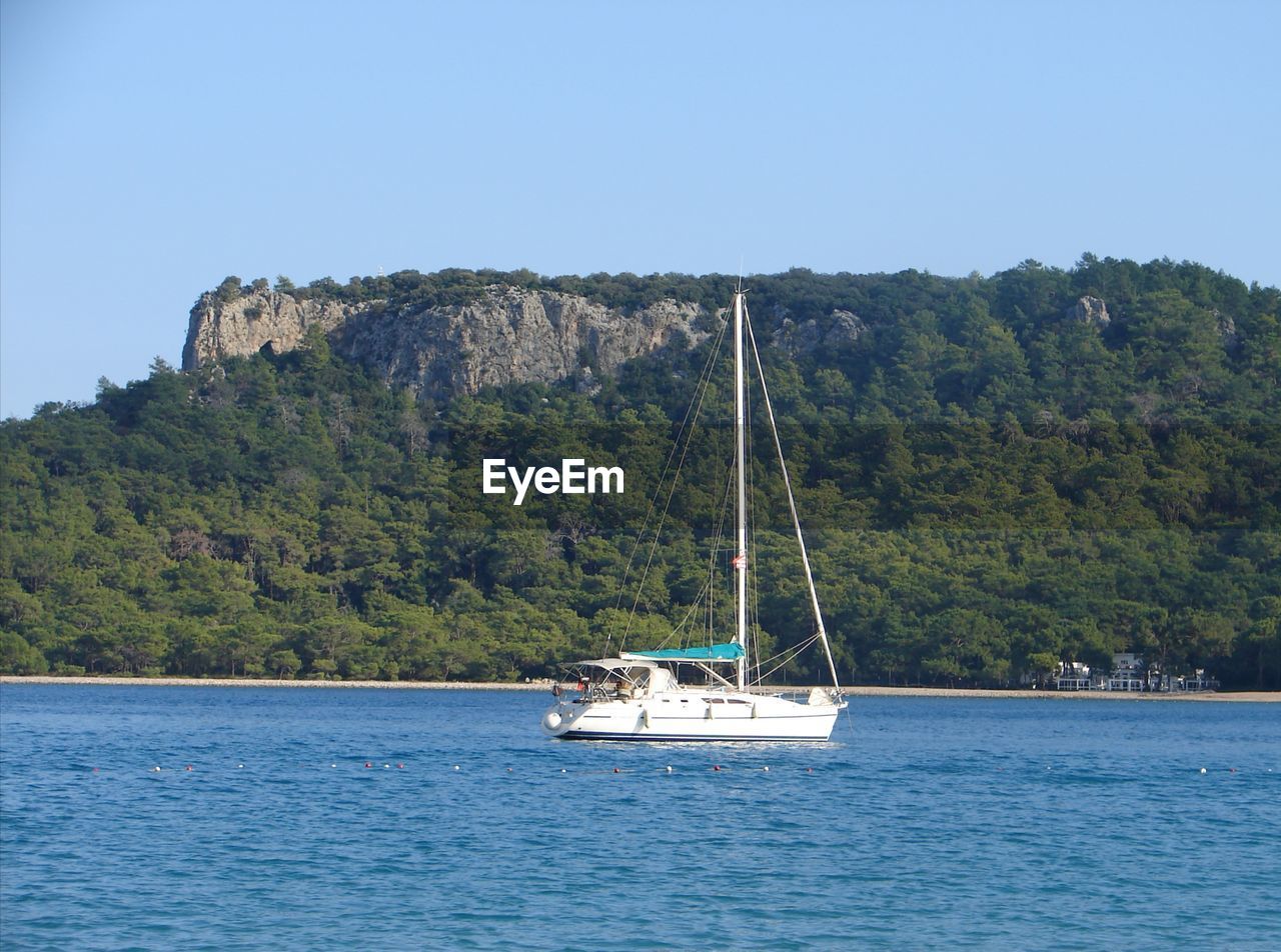 SAILBOAT SAILING ON SEA AGAINST MOUNTAIN