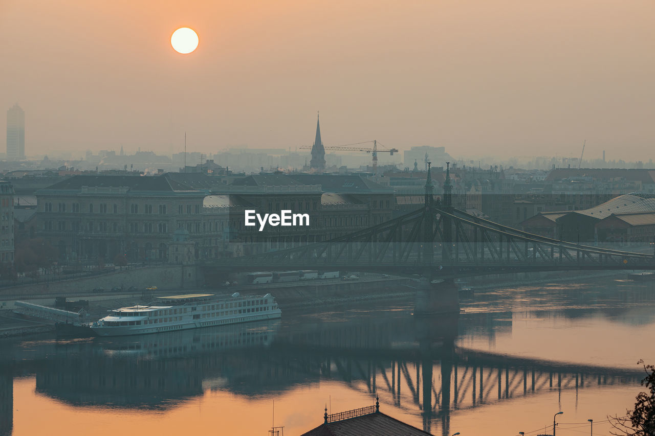 Bridge over river against buildings during sunset