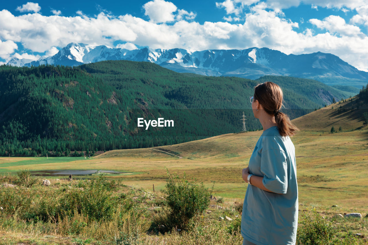 REAR VIEW OF WOMAN STANDING ON LAND AGAINST MOUNTAIN