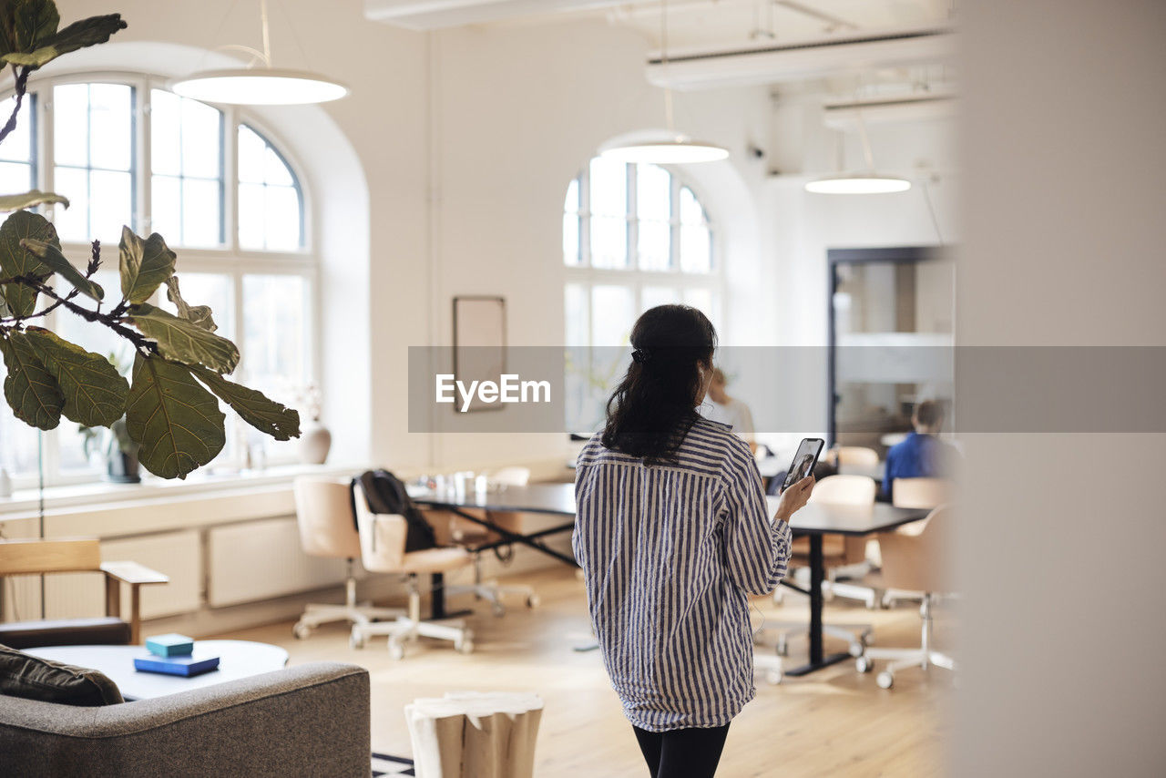 Rear view of female entrepreneur doing video call through smart phone at coworking office