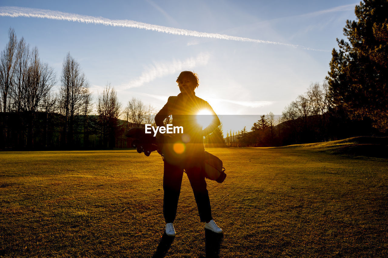 Rear view of man standing on field against sky during sunset