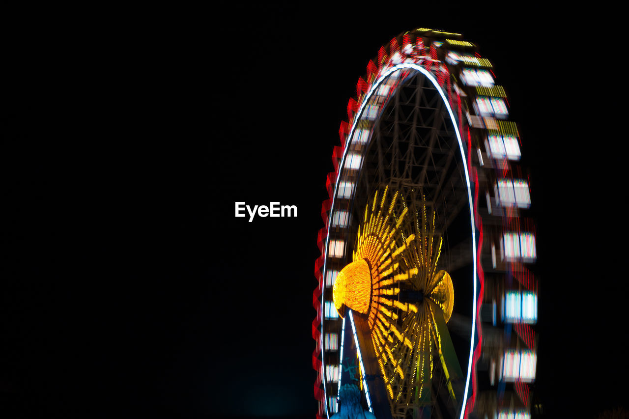 Low angle view of illuminated ferris wheel spinning against sky at night