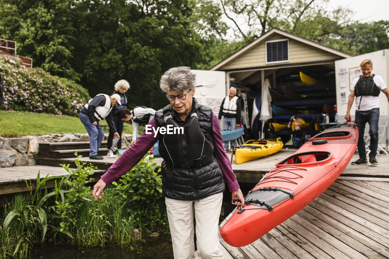 Senior woman and man carrying kayak on jetty during kayaking course