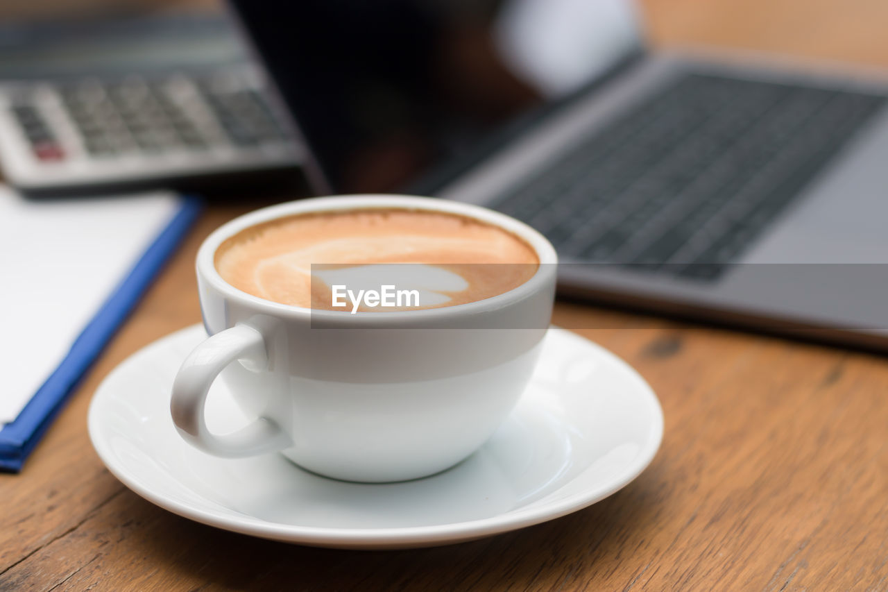 Close-up of coffee cup by laptop on table
