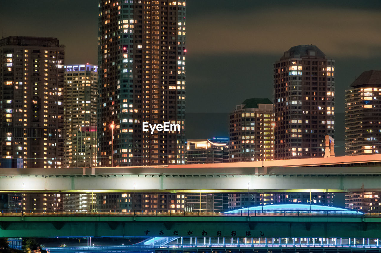 Illuminated modern buildings in city against sky at night