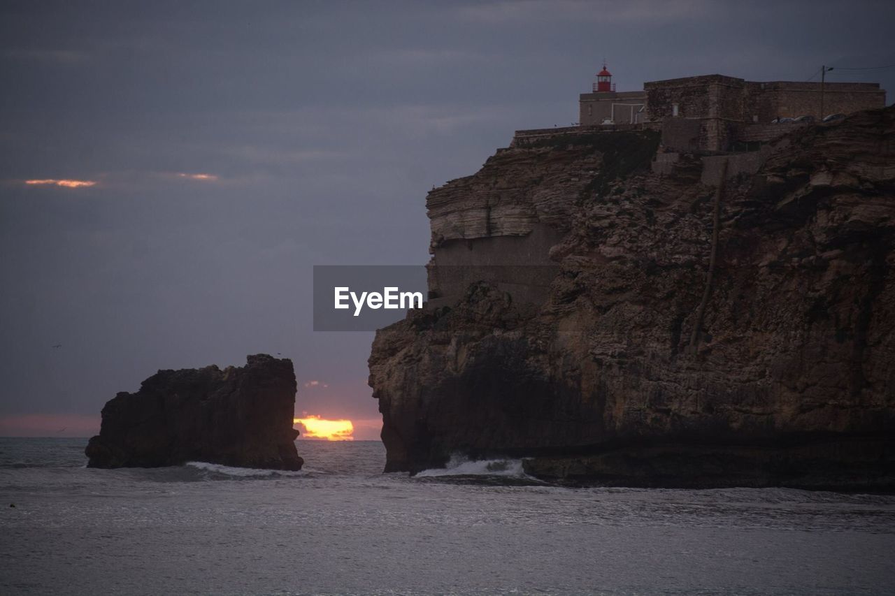 Rock formations by sea against sky at sunset