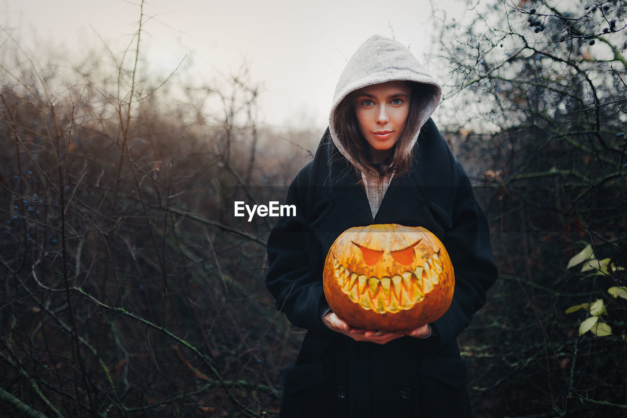 Portrait of woman holding pumpkin in forest during autumn