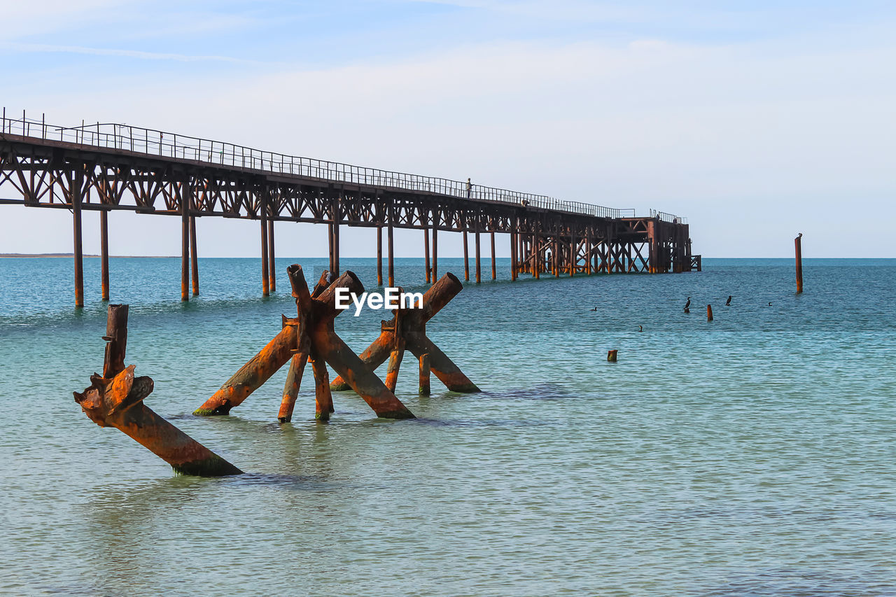 The old long rusty pier going into the sea. there is a man standing on the pier. in the foreground 