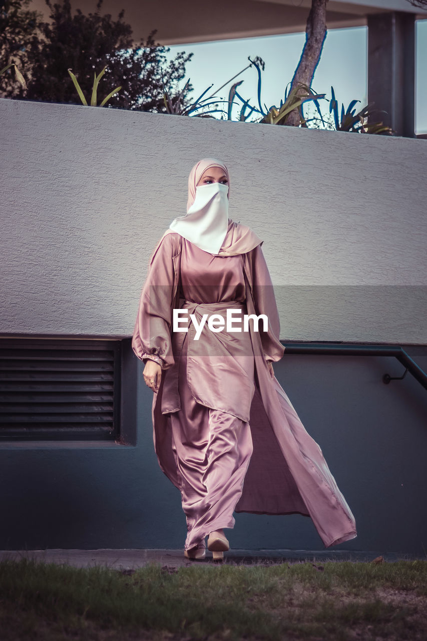 Full length of veiled woman with white niqab and pink silky dress walking towards the camera