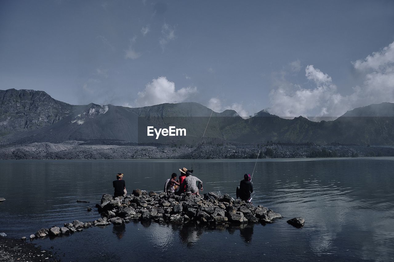 People fishing in lake against mountains