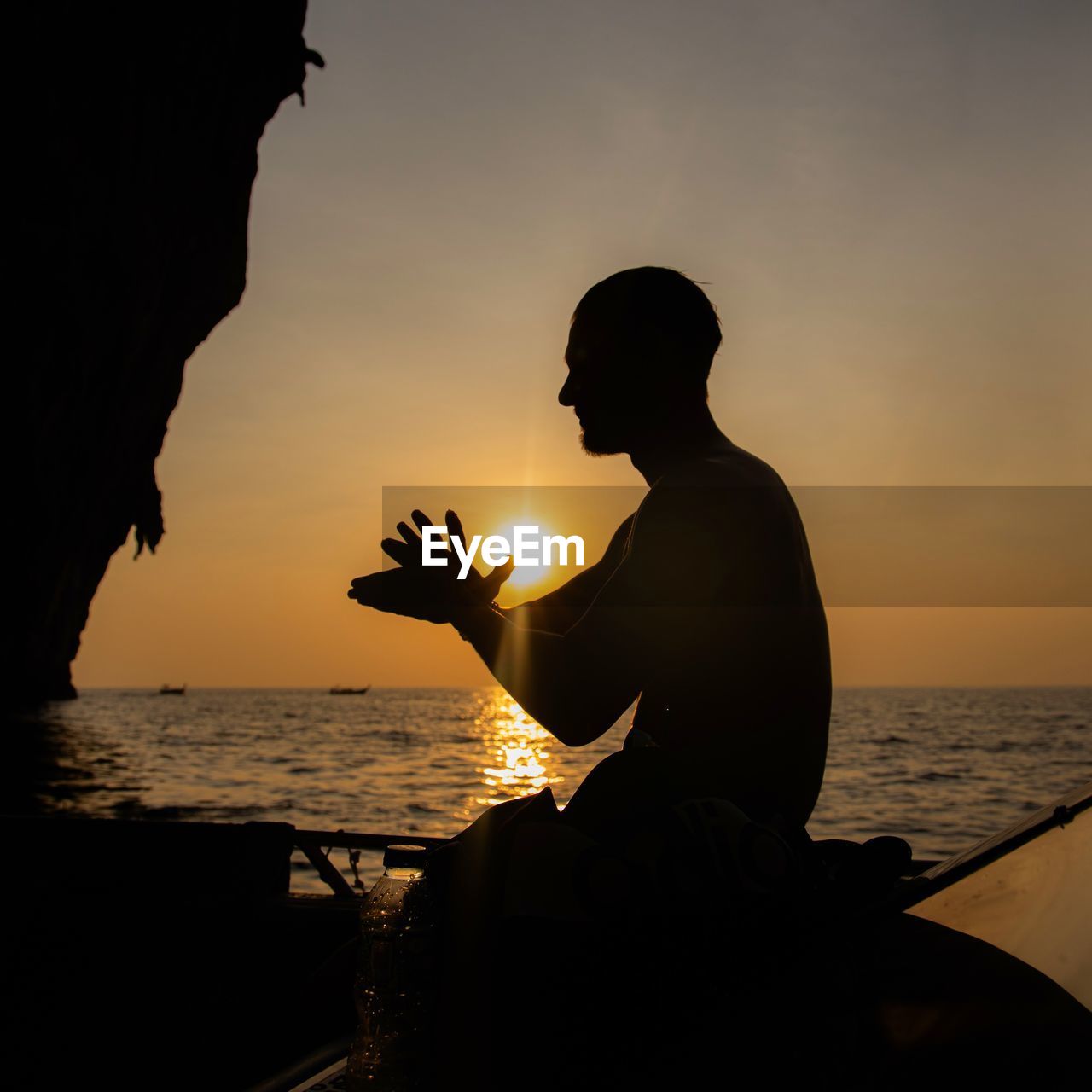 SILHOUETTE MAN SITTING ON BEACH AGAINST ORANGE SKY