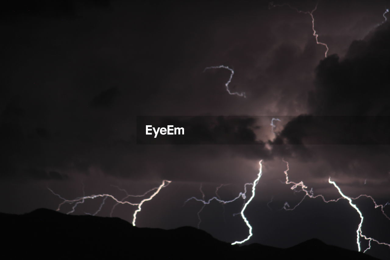 LOW ANGLE VIEW OF LIGHTNING IN SKY OVER SILHOUETTE PEOPLE