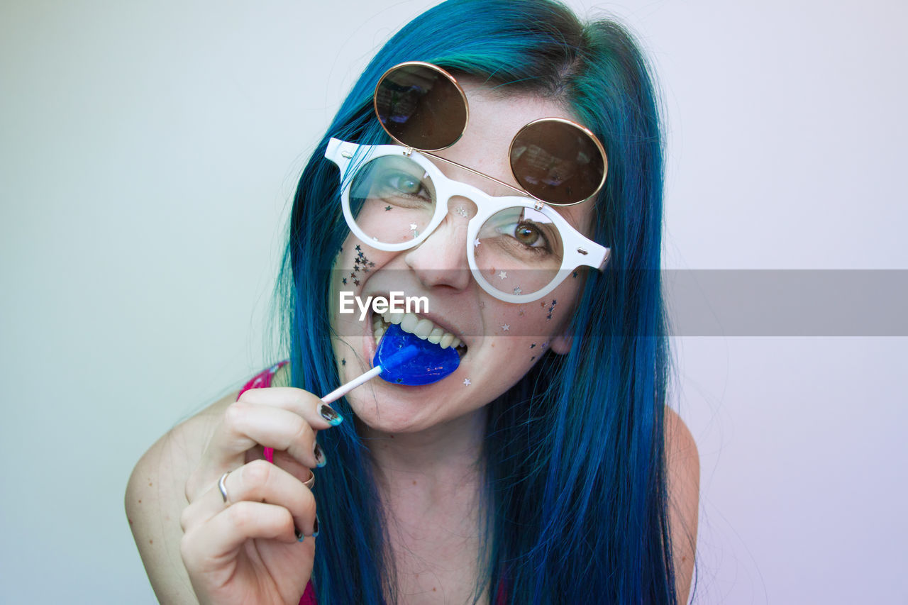 Portrait of woman wearing sunglasses while eating candy against wall