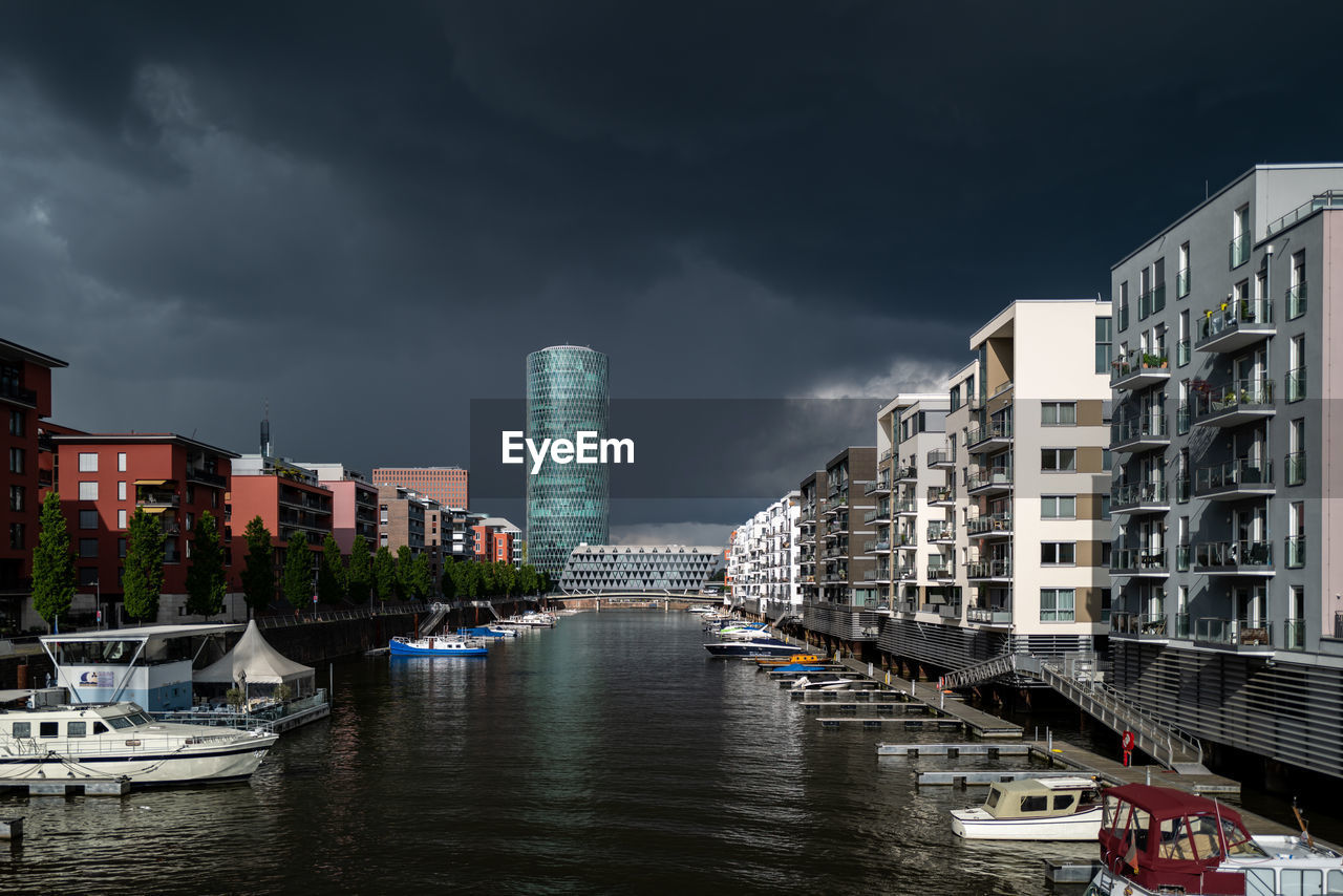 BOATS MOORED ON RIVER BY BUILDINGS AGAINST SKY