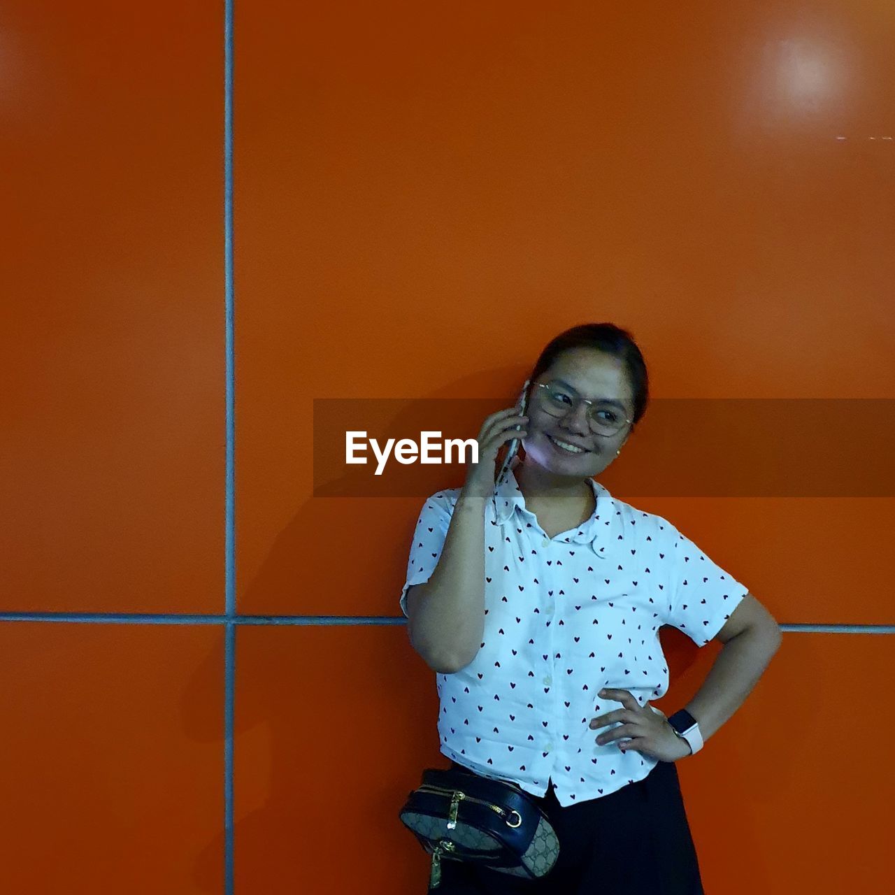 PORTRAIT OF A SMILING YOUNG WOMAN STANDING AGAINST ORANGE WALL