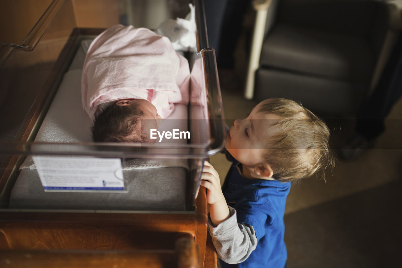 Brother looking at sister sleeping in crib at hospital