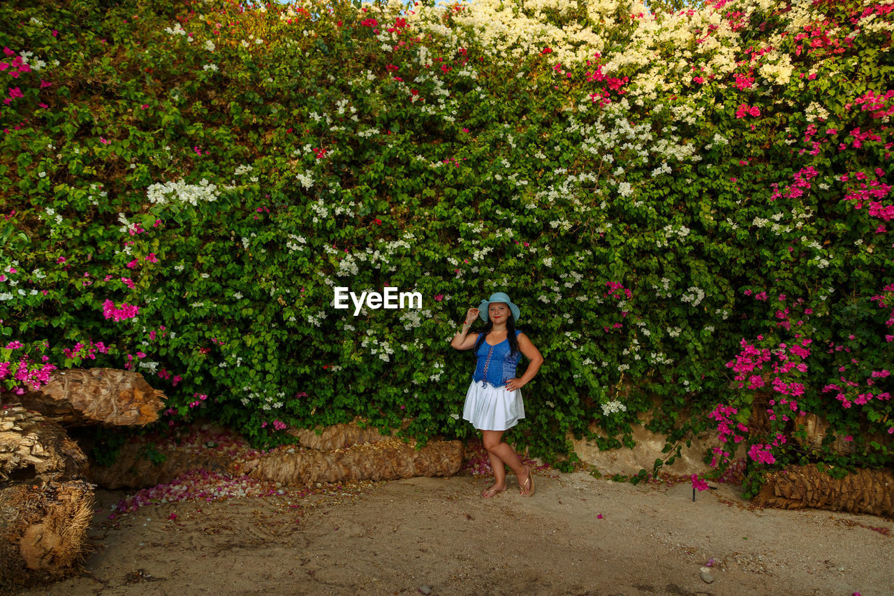 plant, one person, flower, full length, flowering plant, nature, women, beauty in nature, growth, adult, leisure activity, standing, garden, lifestyles, day, casual clothing, young adult, freshness, outdoors, leaf, tree, female, front view, green, pink, walking, fashion, shrub, dress, clothing, person