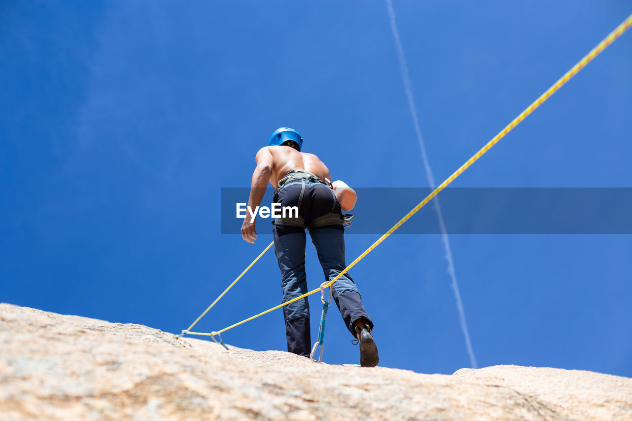 Rear view of shirtless man climbing rock