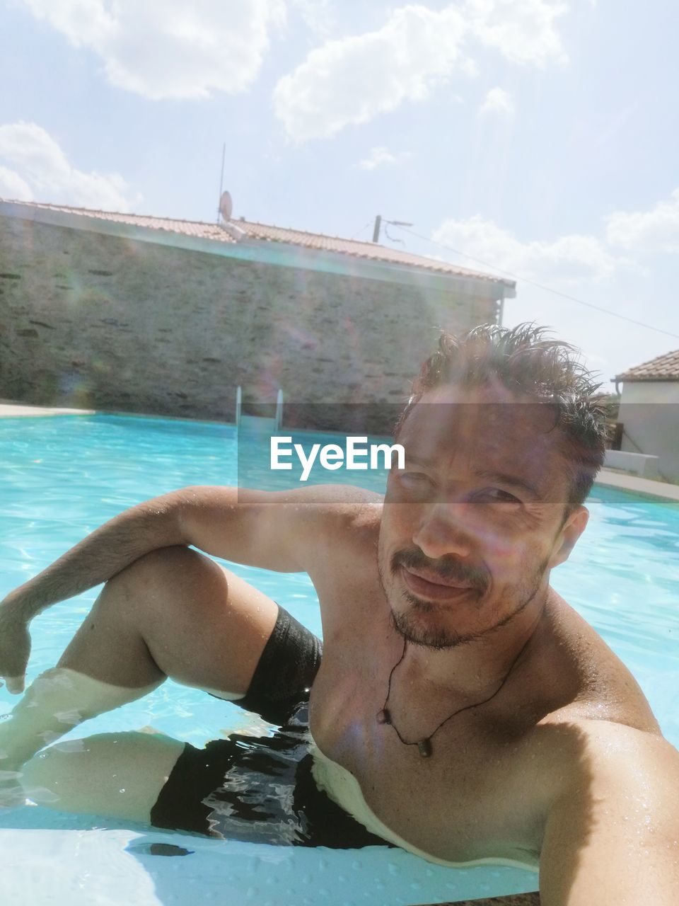 Portrait of shirtless man in swimming pool against sky